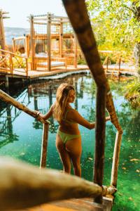 a woman in a bikini standing on a bridge in the water at Hotel Shibari - Restaurant & Cenote Club in Tulum