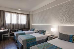 a hotel room with two beds and a desk at Monreale Plus Midtown Campinas in Campinas