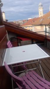 einen Tisch und einen Stuhl auf einem Balkon mit einem Uhrturm in der Unterkunft Appartement de caractère in Gap