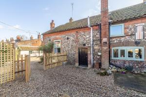 a brick house with a wooden gate and a fence at Greyhound Cottage in Sculthorpe