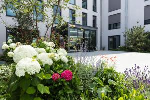 ogród z białymi i różowymi kwiatami przed budynkiem w obiekcie SOLLER Business Hotel - Munich Airport MUC w mieście Hallbergmoos