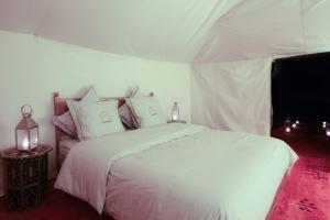 una camera da letto con un letto bianco con lenzuola e cuscini bianchi di Bivouac de Luxe Le Pacha a M'Hamid