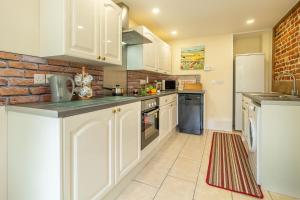 a kitchen with white cabinets and a brick wall at Margarets Cottage in Potter Heigham