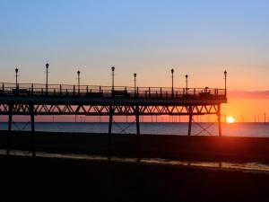a pier at the beach with the sunset in the background at Ellas Apartment in Skegness