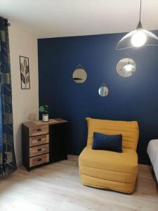 1 dormitorio con silla amarilla y pared azul en Aux cocons Précignéens : Studio Bleuet, en Précigné