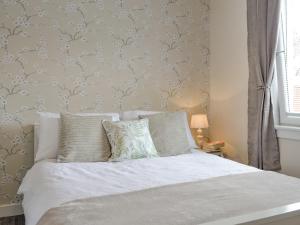 Honeysuckle Cottage في Luncarty: غرفة نوم بسرير مع شراشف بيضاء وجدار