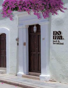 Un bâtiment blanc avec une porte marron et des fleurs violettes dans l'établissement Noma Bed & Breakfast, à San Cristóbal de Las Casas