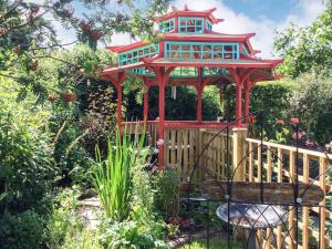 a red gazebo with a bench in a garden at Spa Cabin in New Milton