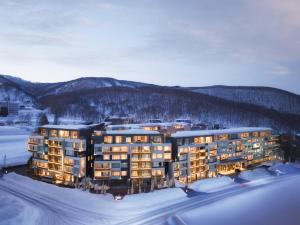 un grand bâtiment dans la neige avec les montagnes dans l'établissement Setsu Niseko, à Niseko