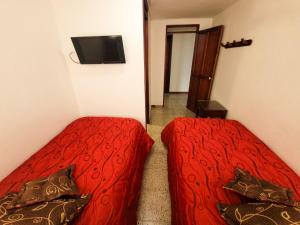 Hotel Paucura في Pácora: غرفة نوم بسريرين مع شراشف حمراء وتلفزيون