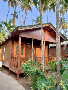 a wooden house with palm trees in front of it at Tranquil Beach Resort in Harihareshwar