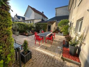 un patio con mesa, sillas rojas y plantas en La suite du Theatre en Bourges