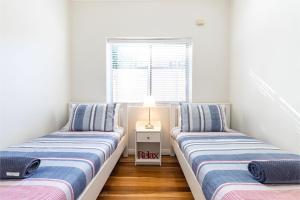Dos camas individuales en una habitación con ventana. en Tomaree Cottage 12 Tomaree Road - 200 mtrs to Beach - Pet Friendly, linen, WiFi & aircon, en Shoal Bay