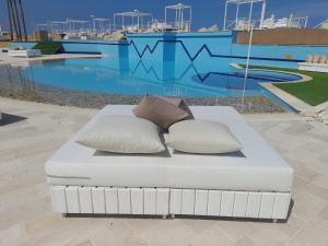 a white couch with two pillows in front of a pool at Four Seasons Halat in Jbeil