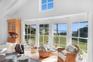 a living room with a couch and chairs and windows at White Shell Cottage - Woodfire & Beachfront in Falmouth