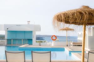 a swimming pool with chairs and a straw umbrella at Beach Club Menorca in Son Parc