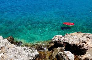a red boat in the water next to some rocks at Rustic Stone House in the Heart of Folegandros in Áno Meriá