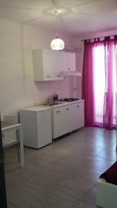 une cuisine avec des placards blancs et un rideau rose dans l'établissement Case vacanze Iris, à Uggiano la Chiesa