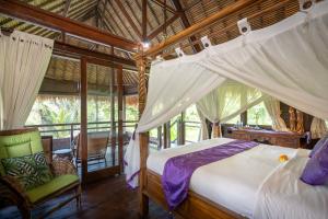 a bedroom with a canopy bed and a chair at Kupu Kupu Private Villa in Ubud