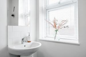 un baño con lavabo y un jarrón de flores en una ventana en Spacious 4 Bedroom house near Leeds CC, en Beeston Hill