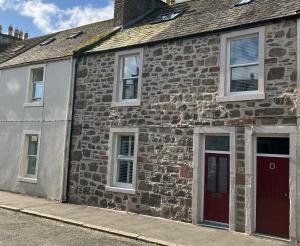 an old stone house with a red door on a street at Serendipity in Kirkcudbright