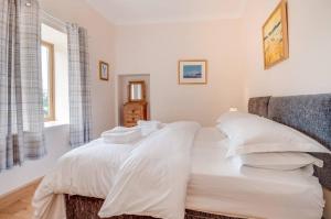uma cama com lençóis brancos e almofadas num quarto em Kinnen Cottage em Creetown