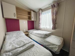 two beds in a small room with a window at Modern Caravan With Decking At Azure Seas Along The Suffolk Coast Ref 32065az in Lowestoft