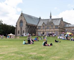 un grupo de personas sentadas en el césped frente a un gran edificio en Ushaw Historic House, Chapels & Gardens en Durham