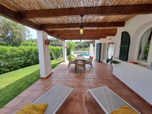 a patio with a table and chairs under a wooden pergola at Villa Xalina - Piscina / bbq / jardín in Fornells