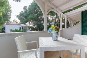 een witte tafel en stoelen op een veranda met een vaas met bloemen bij Appartamento Iremar C1 - MyHo Casa in Vieste