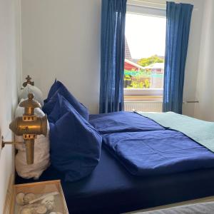 Schlafzimmer mit einem Bett mit blauer Bettwäsche und einem Fenster in der Unterkunft Esther in Norddorf