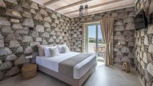 a bedroom with a large bed and a stone wall at Thea Sunset Suites in Mytakas