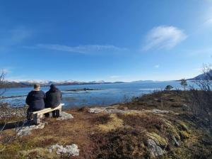 duas pessoas sentadas num banco a olhar para a água em Cottage with seaview em Lodingen