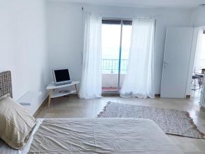 Ein weißes Zimmer mit einem Bett und einem Laptop auf einem Tisch. in der Unterkunft Appartement en bord de mer in Pietranera