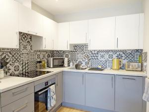 a kitchen with white cabinets and a tile wall at Pebblestone in East Wittering