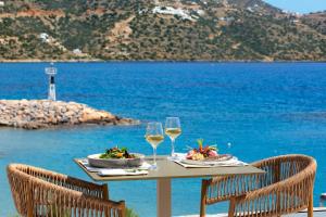 a table with two glasses of wine and food on the beach at Wyndham Grand Crete Mirabello Bay in Agios Nikolaos