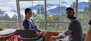 a man and woman sitting in a room with a view of mountains at Rohana Estate Lodging & Camping in Kandy