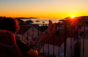 una persona sentada en un balcón con vistas a la puesta de sol en Apartments Viskovic, en Hvar