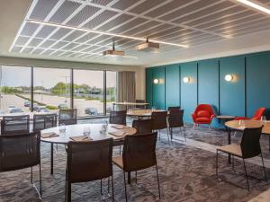 a dining room with tables and chairs and windows at Novotel Cambridge North in Cambridge