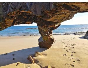 una formazione rocciosa su una spiaggia con impronte sulla sabbia di Apartamento Playa Foz a Foz