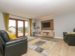 a living room with two leather chairs and a flat screen tv at Bumble Bee Retreat in Axminster