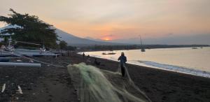 a person standing on a beach with a net at Amed Sari Beach Guesthouse in Amed