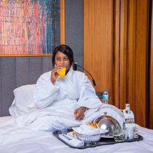 a woman sitting in a bed drinking a glass of juice at Radisson Blu Hotel & Conference Center, Niamey in Niamey