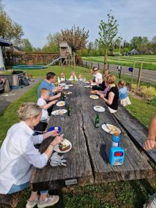 un grupo de personas sentadas en una mesa de picnic de madera en De Slaapfabriek vakantiehuis en trainingslocatie, en Teuge