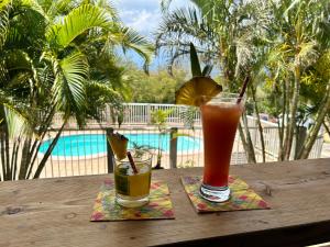 dos bebidas sentadas en una mesa de madera junto a una piscina en Gîtes Hotel Couleur Caraibes, en Bouillante