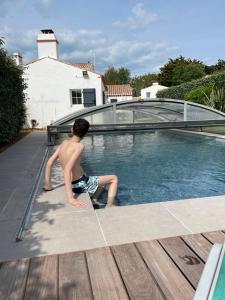 um rapaz sentado à beira de uma piscina em Chambres d'hôtes LES CHENES VERTS em Le Grand Vieil