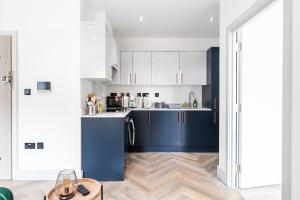 a kitchen with blue and white cabinets and a wooden floor at Livestay-Modern Apartments in Romford near Elizabeth Line in Romford