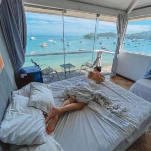 een vrouw op een bed met uitzicht op de oceaan bij Bamboo Búzios Hostel in Búzios