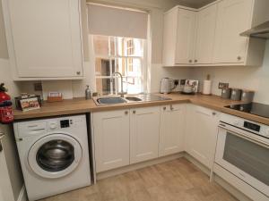 a kitchen with white cabinets and a washing machine at Charter's Cottage in Berwick-Upon-Tweed
