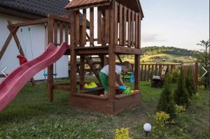 a man playing in a wooden playground with a slide at Solina domki-„Solińskie wzgórze” in Solina